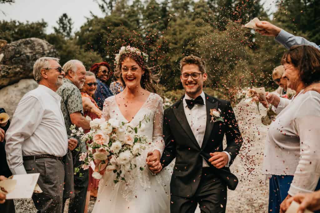 a bride and groom holding hands having dried flower confetti tossed on them