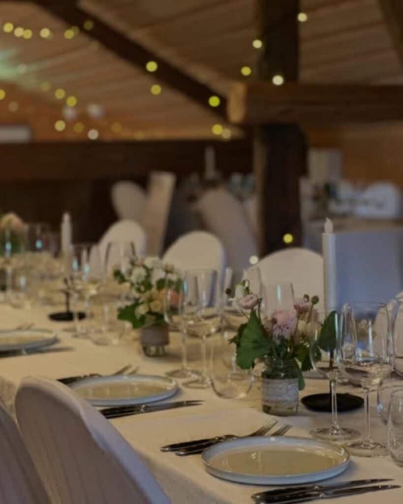 long table with flowers and fine cutlery for a party with twinkle lights in the background