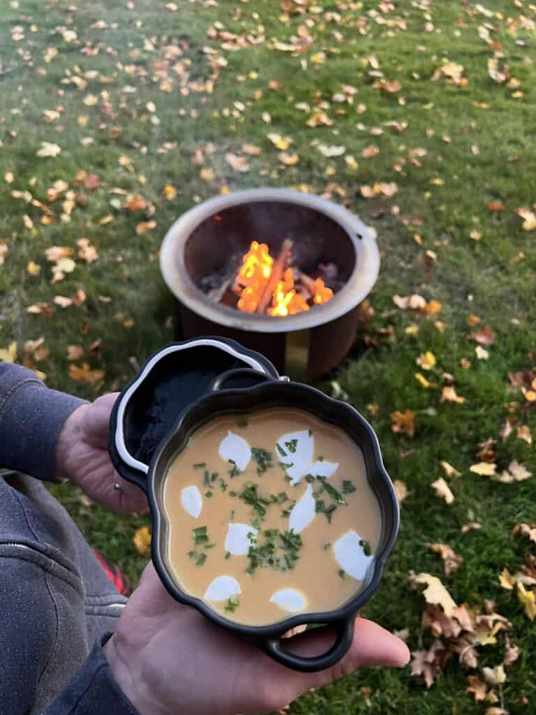 pumpkin soup in a pumpkin bowl with a firepit on the grass in the background