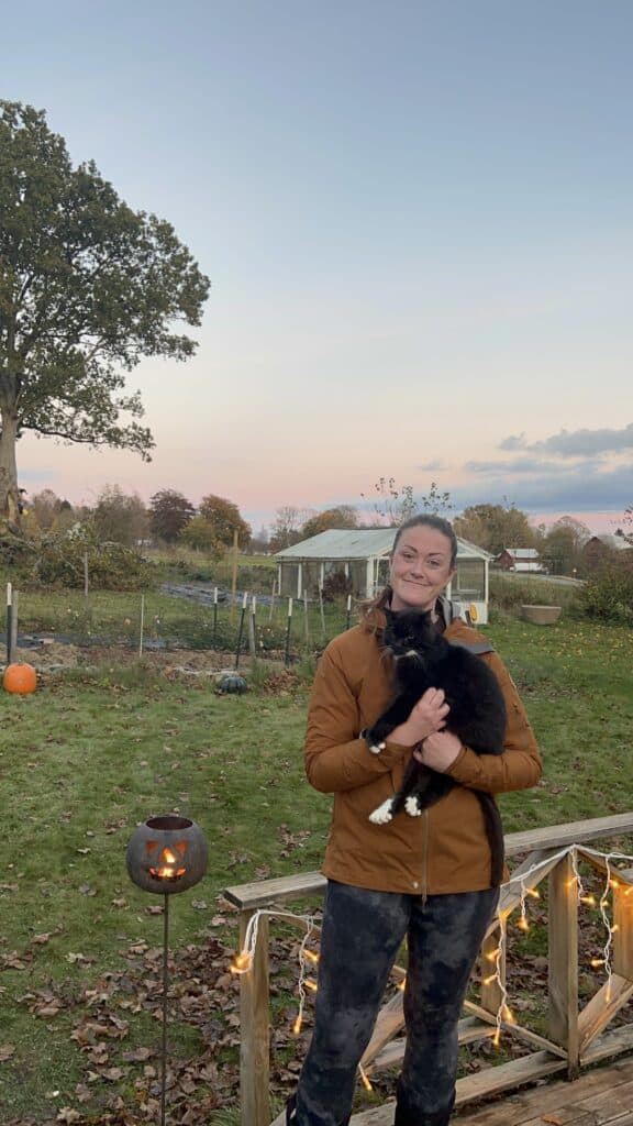 woman holding a black cat with the sunset and garden in the background