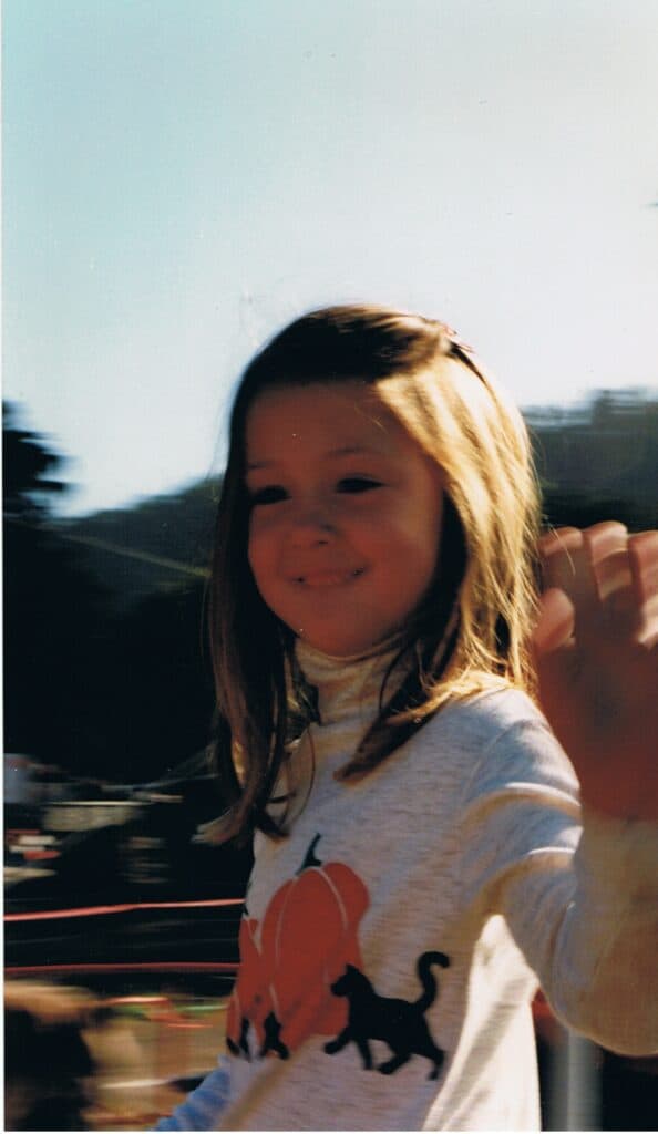 little girl in a pumpkin and cat shirt waving