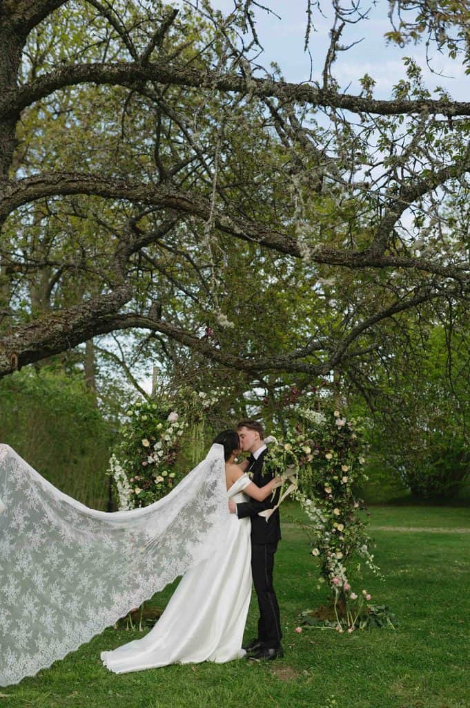 bride and groom kissing in front of a floral arch